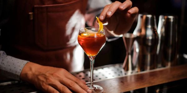 Bartender garnishing a cocktail with an orange peel at a bar.