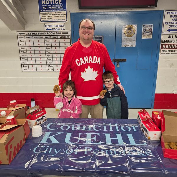 Man and two kids smiling behind a politician's table with snacks.