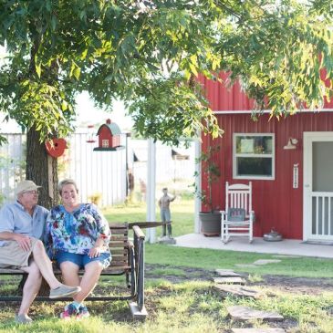 Couple sitting on a swing under a tree near a red house.