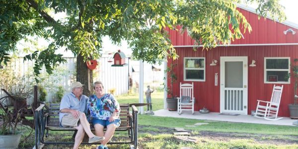 Couple sitting on a swing under a tree near a red house.