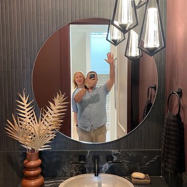 The founder, Hannah, and her husband, Dennis posing for a photo in a mirror above a sink at a house e