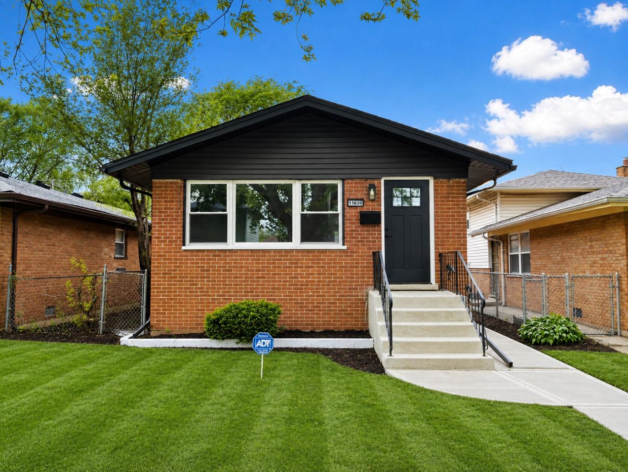 Small brick house with a black door and manicured lawn.
