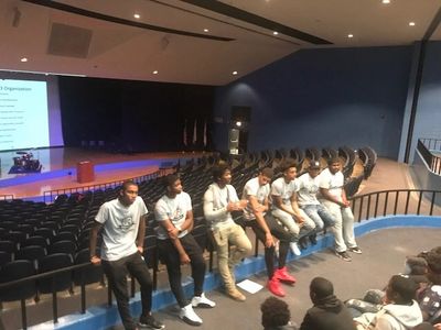 Group of young men sitting on a ledge in an auditorium.