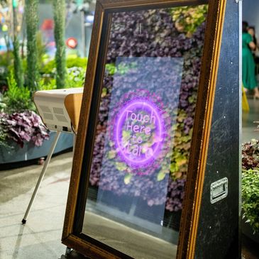 Interactive touchscreen mirror with a camera and lighting setup in a greenhouse setting.