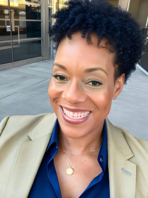 Smiling woman with curly hair wearing a beige blazer and blue shirt.