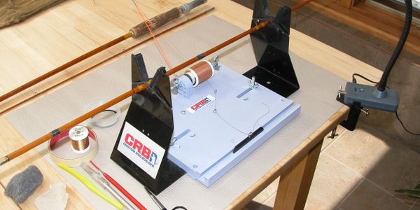 A fishing rod building setup on a wooden table with tools and materials.