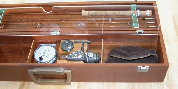 Open wooden fishing tackle box with reels and rod compartments.
