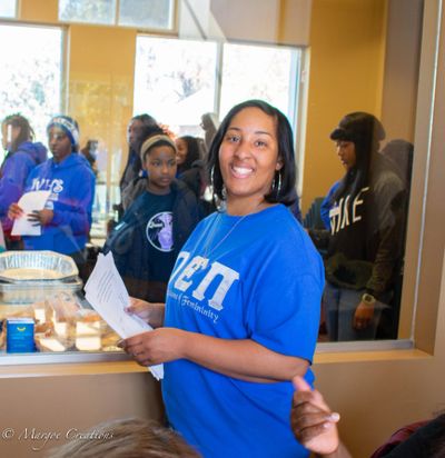 Smiling woman in blue shirt holding papers at a community event.