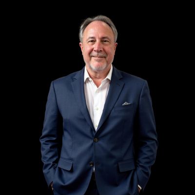 Smiling man in navy blue suit against a black background.