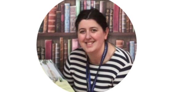 Smiling woman with dark hair in a striped shirt, sitting in front of a bookshelf.
