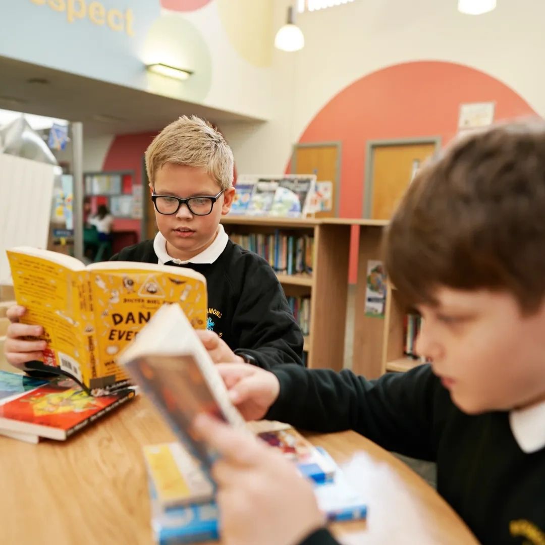 Two boys reading books in a colorful school library.
