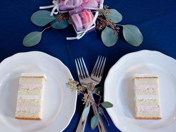 Two slices of layered cake on white plates with forks and eucalyptus decoration.