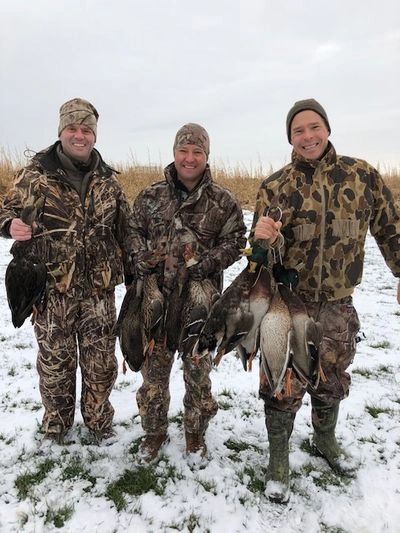 Three hunters in camouflage holding ducks they hunted in snowy field.