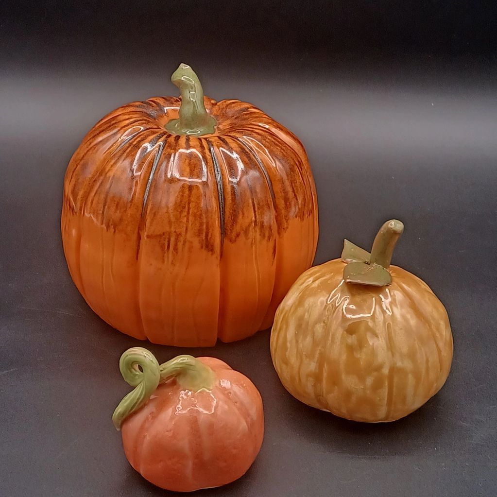 Three hand-built pottery pumpkin sculptures in a variety of orange colors.