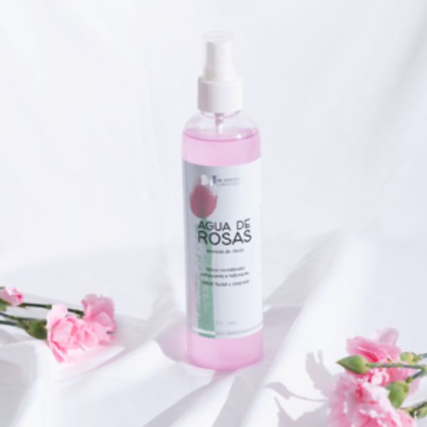 Botella de agua de rosas con flores rosas sobre tela blanca.
