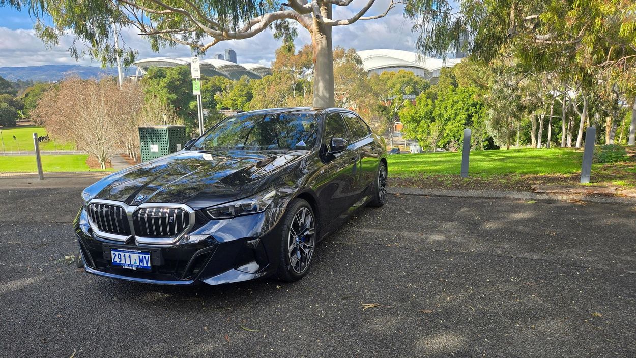 Black BMW parked on an asphalt near green trees and stadium.