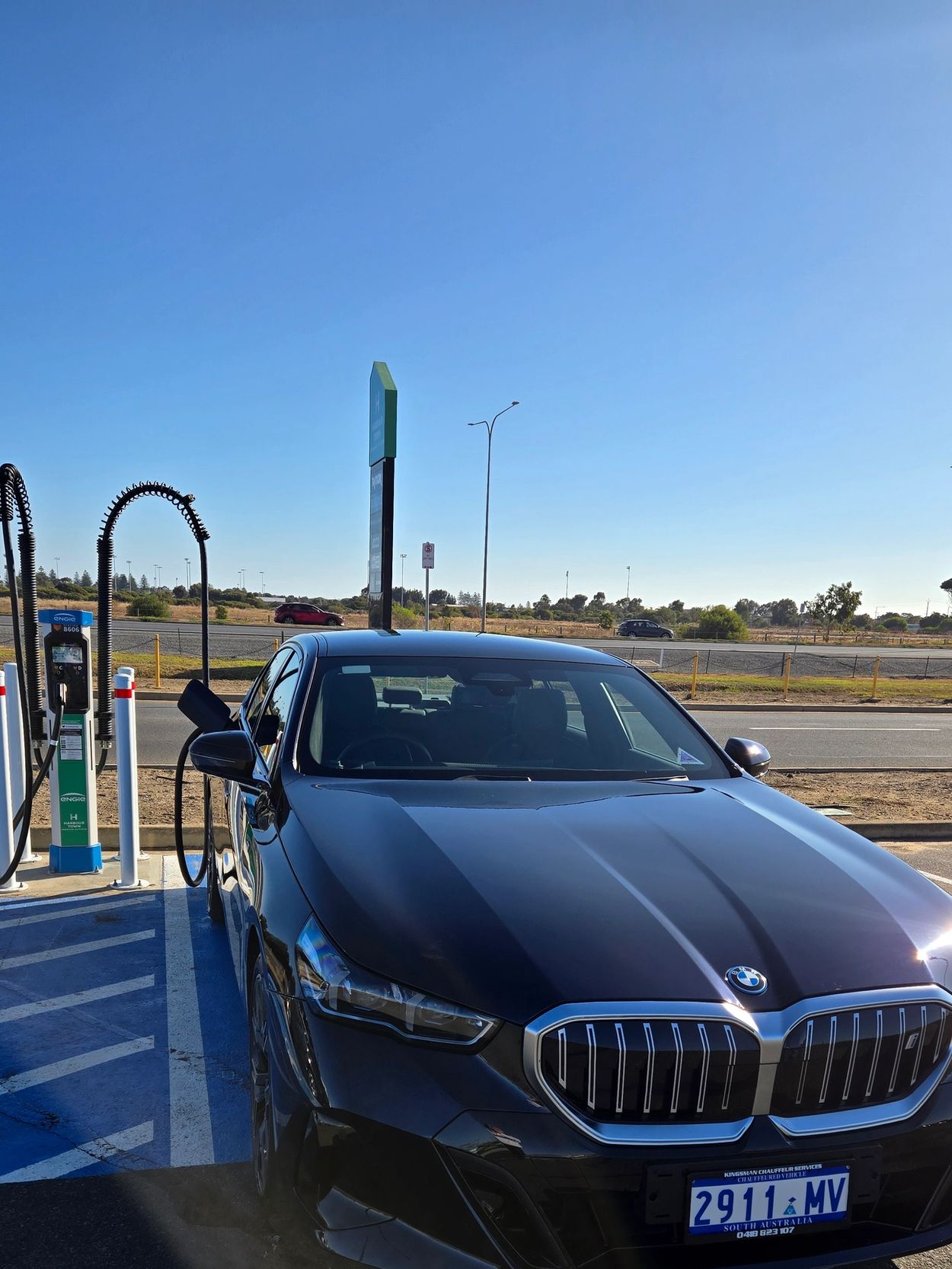 Black BMW charging at a hydrogen fuel station under clear blue skies.