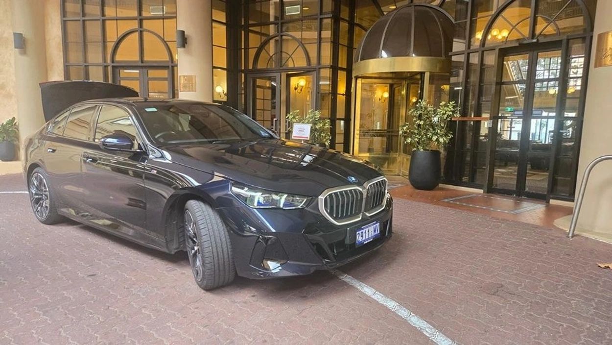 A black BMW sedan with front wheels turned, parked at an entrance with glass doors.