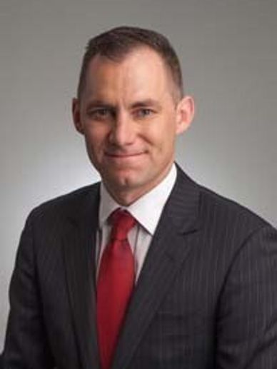Professional man in a dark suit and red tie smiling.
