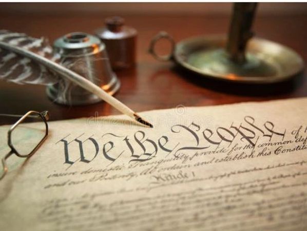 Partial picture of the Constitution saying "We the People" with candle, ink pen, glasses.