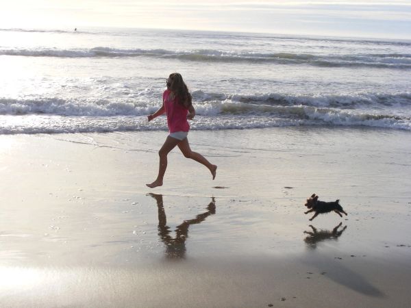 Girl running on the beach with a small dog.