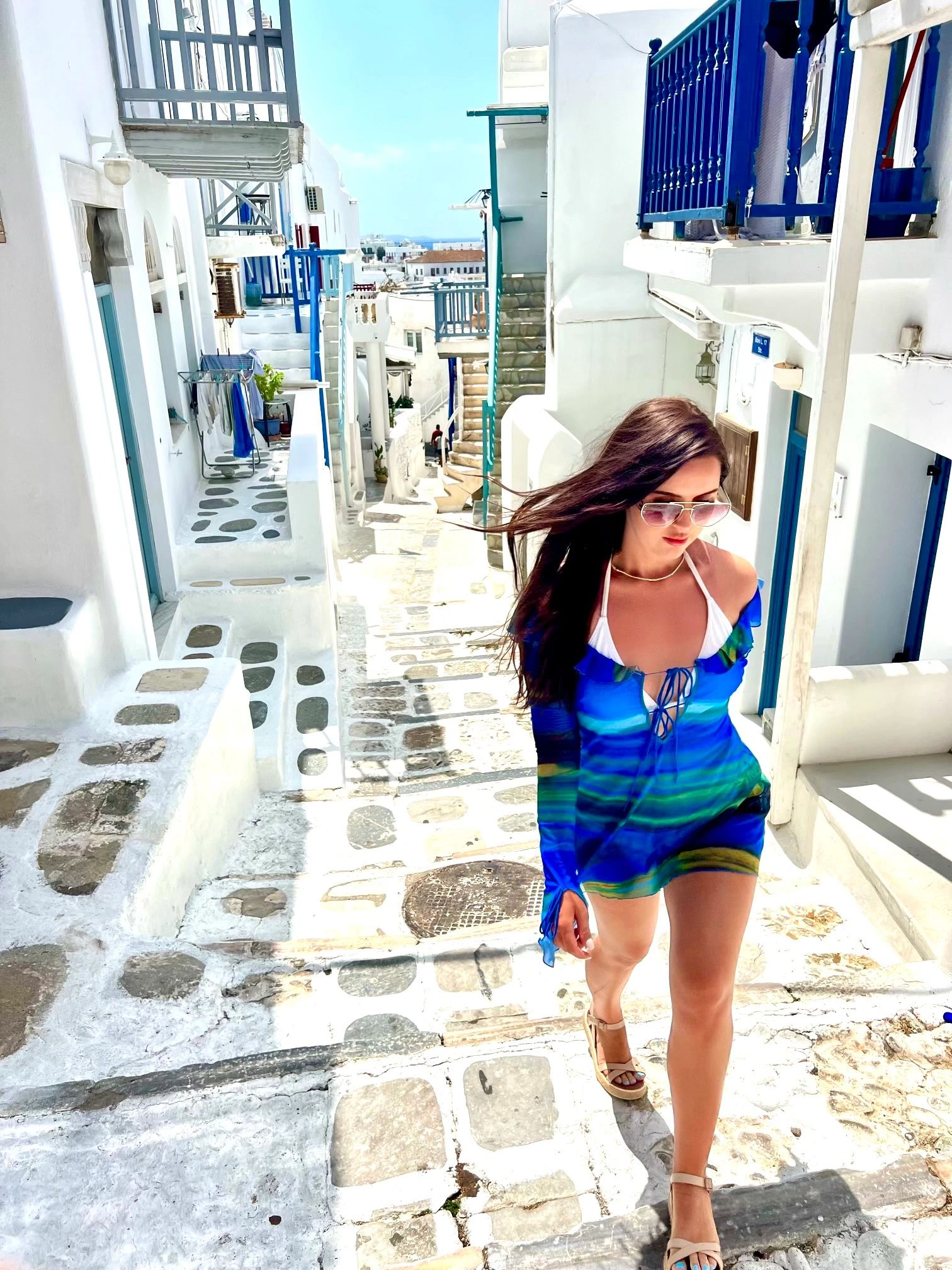 Woman in blue dress walking up sunny steps in a white-washed Mediterranean town.