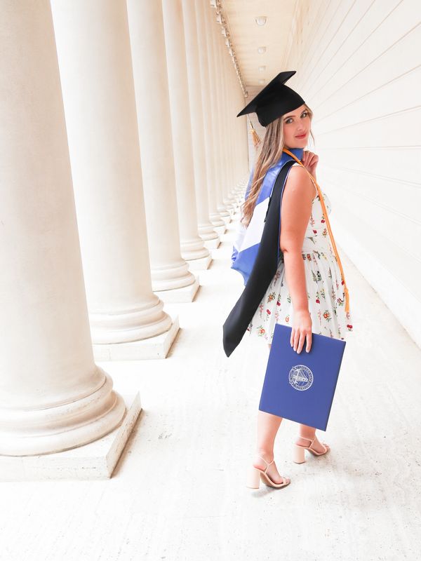 Graduate posing with diploma in elegant corridor.