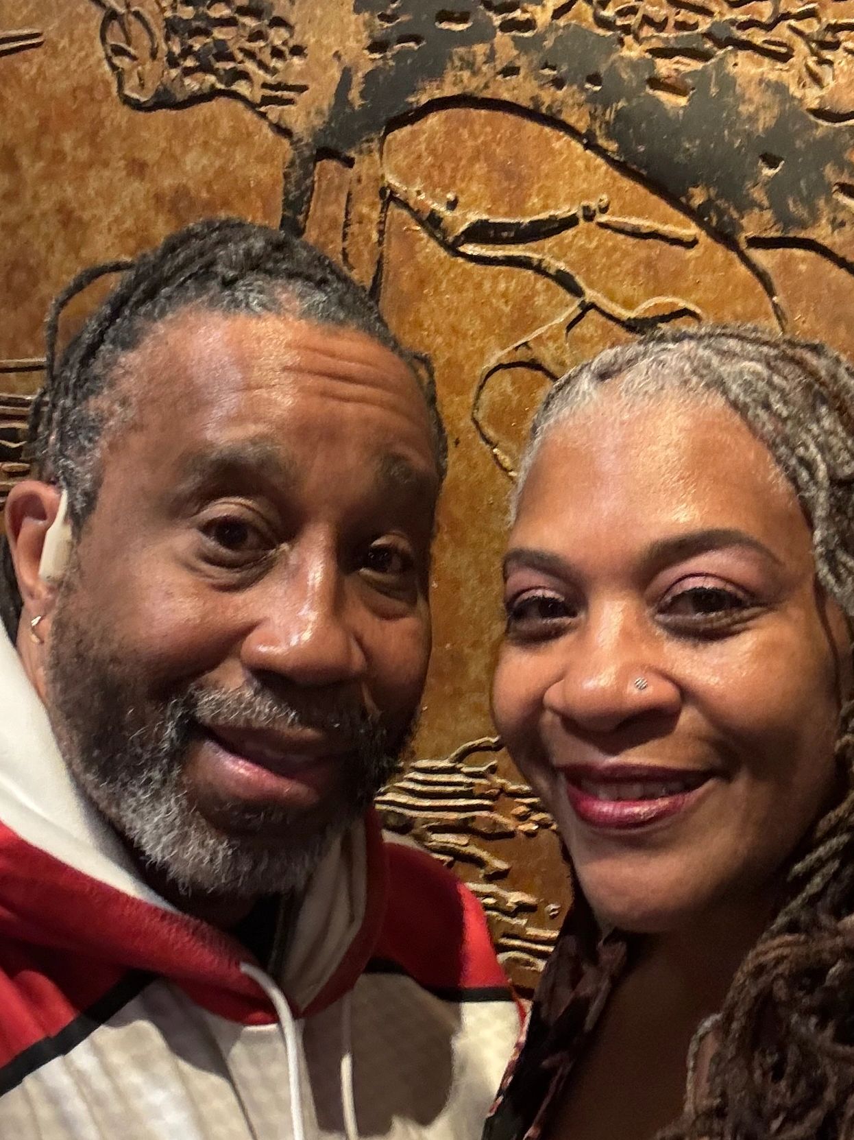 Close-up selfie of a smiling couple with textured wall art background.