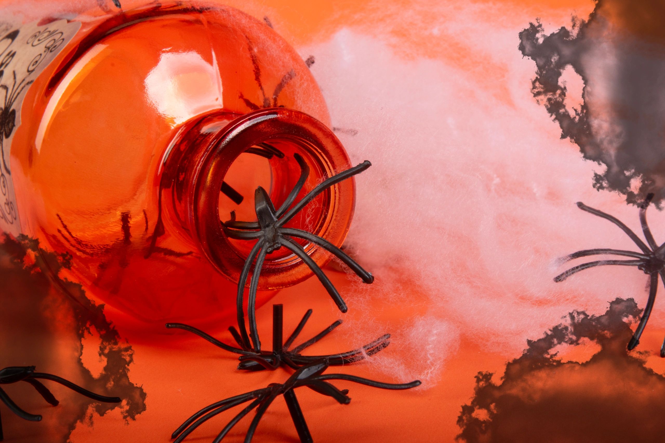 Halloween-themed orange bottle with fake black spiders and cobwebs.