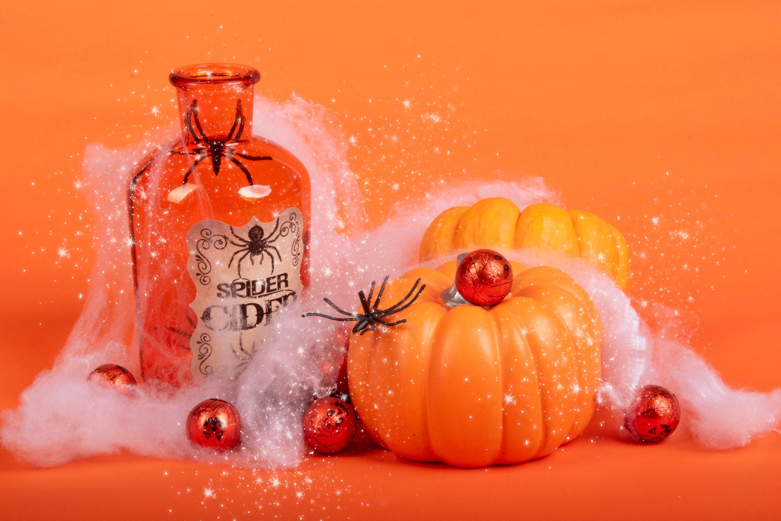 Halloween-themed orange bottle, pumpkins, and spider decorations with a magical sparkle effect.