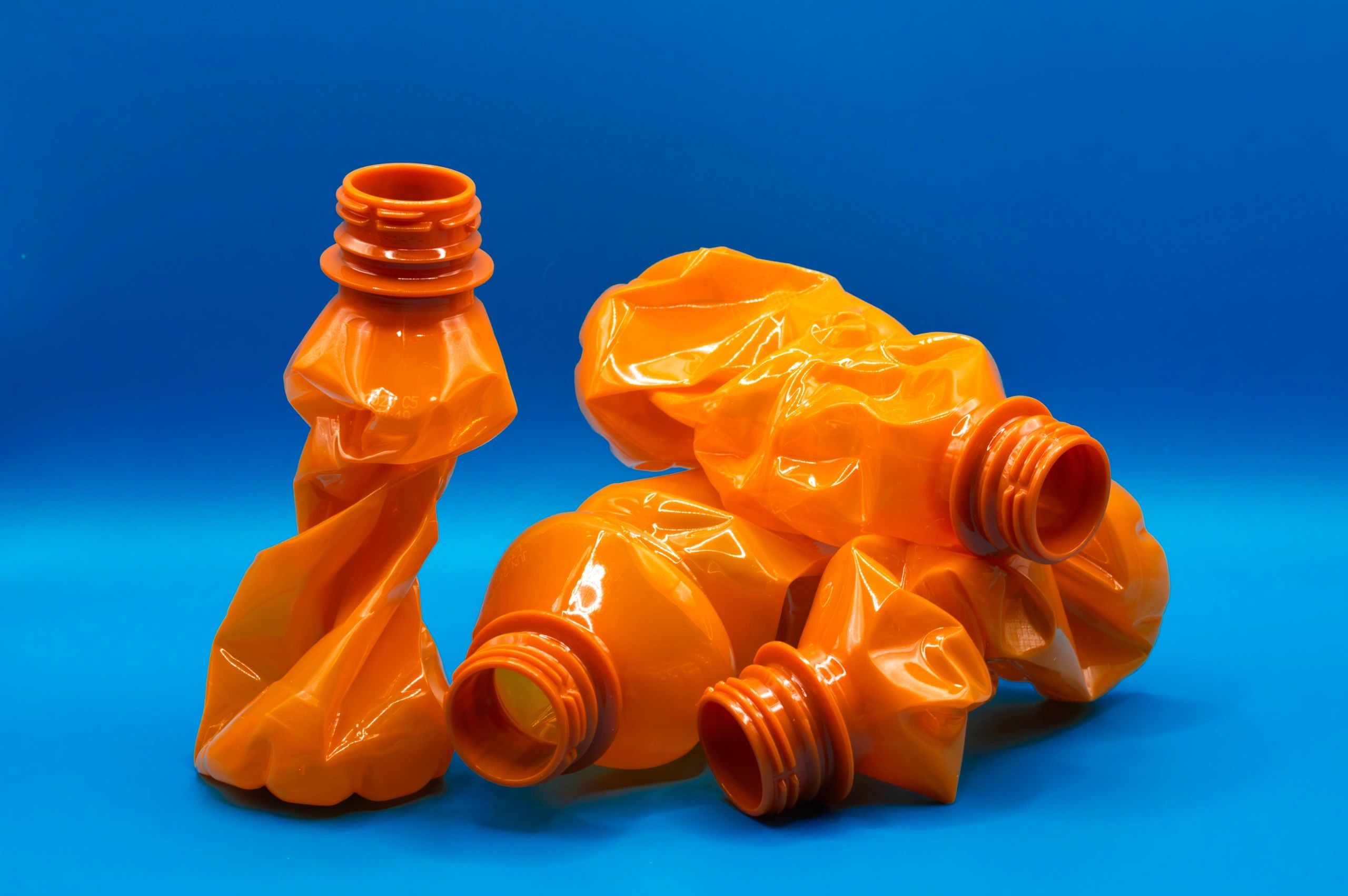 Crumpled orange plastic bottles against a vibrant blue background.
