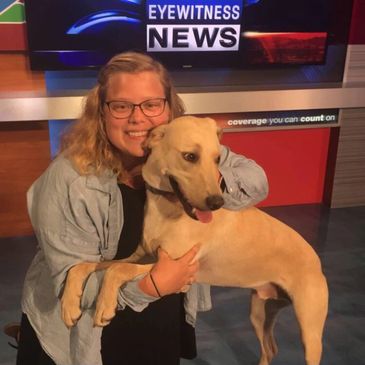 Former University of West Georgia students pictured in front of a WRCB-TV sign, hugging a dog.