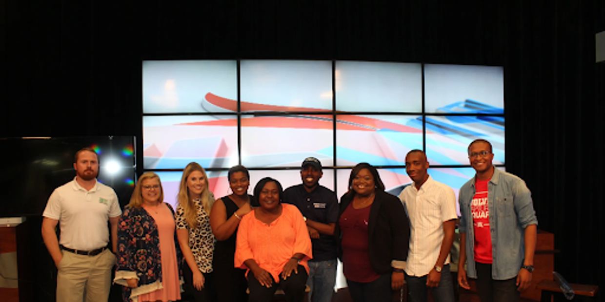 A diverse group of colleagues pictured together in front of a multi-screen digital display.