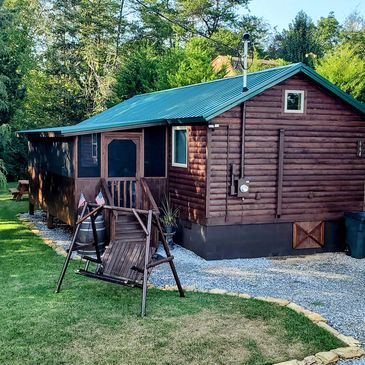 Cozy wooden cabin with a green metal roof and a swing in the yard.