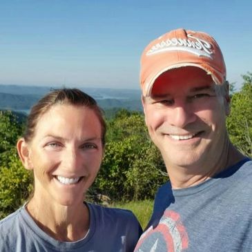 Smiling couple outdoors with scenic background on a sunny day.