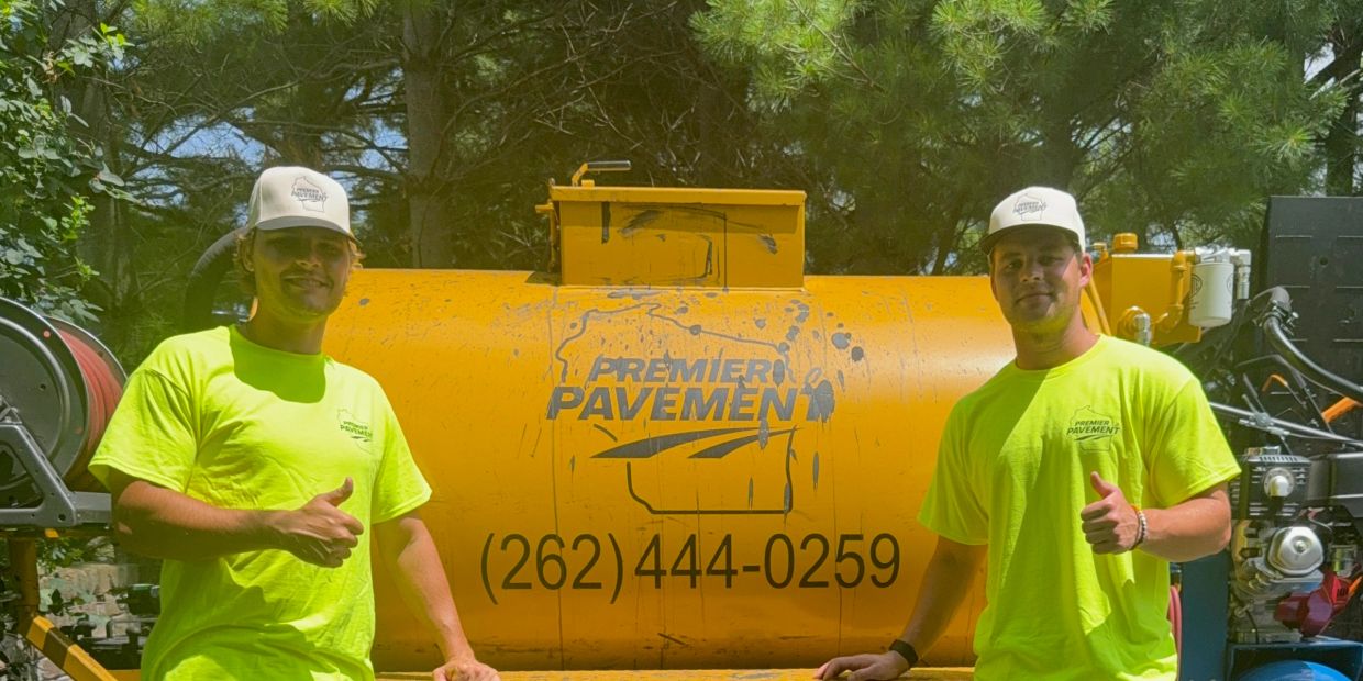 Two men in neon shirts thumbs up by paving equipment.