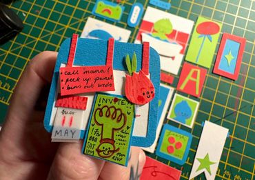 Hand holding a colorful paper craft with various small paper pieces.