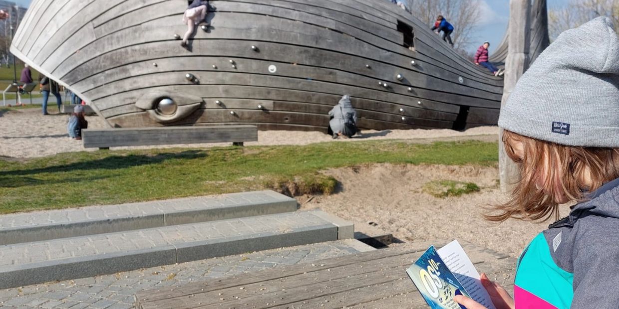 Child reading Oslo at playground with whale in background.