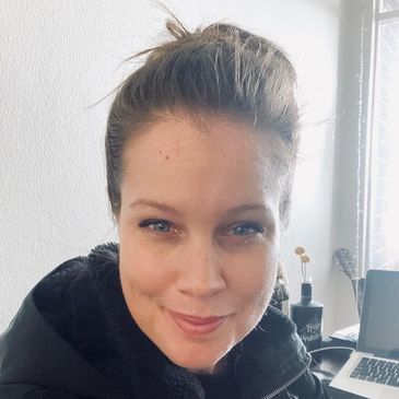 Smiling woman with blue eyes wearing a black jacket indoors.
