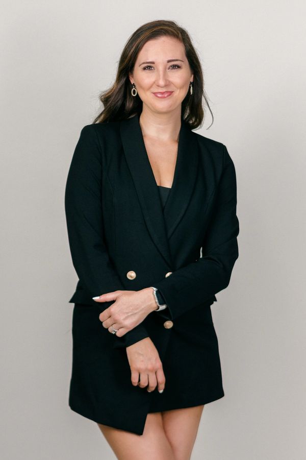 Confident woman in a black blazer dress posing against a plain background.