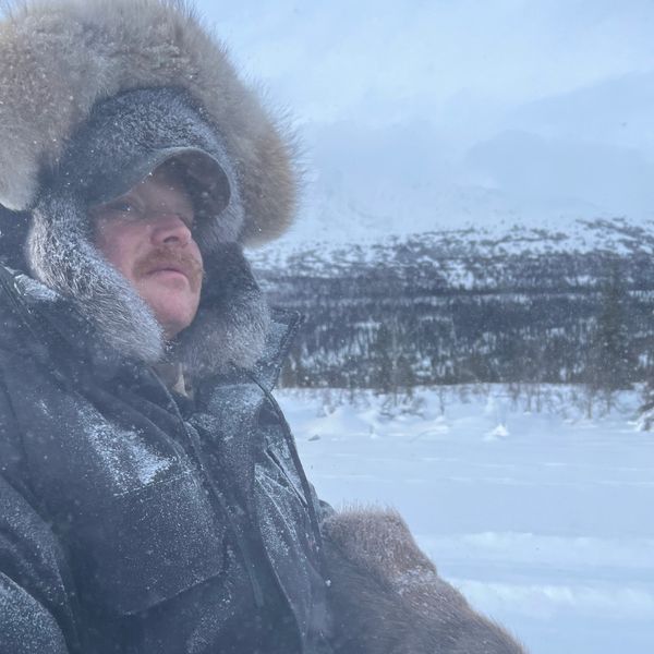 Man bundled in fur-lined winter coat in snowy landscape.