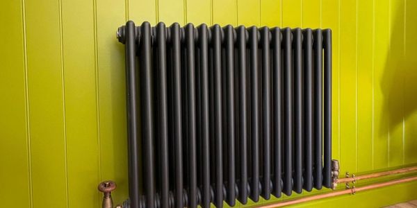 Black radiator mounted on a bright green paneled wall with copper pipes.