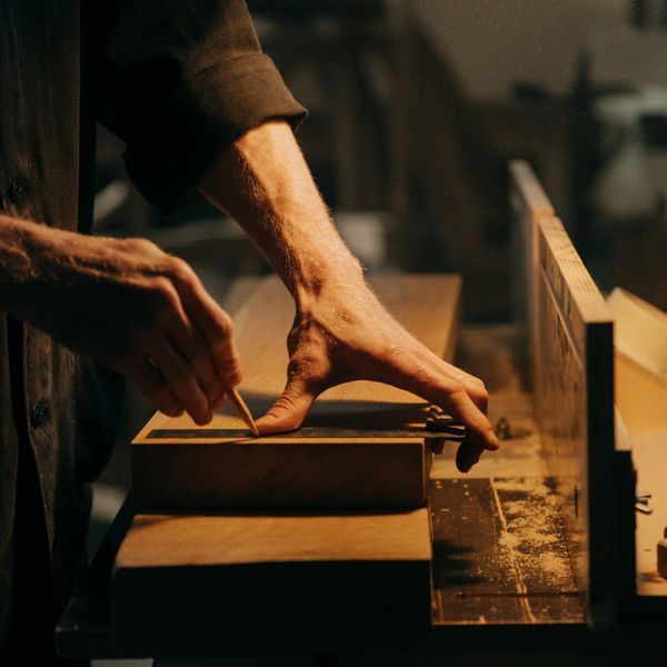 A person marking wood with a pencil in a dimly lit workshop.