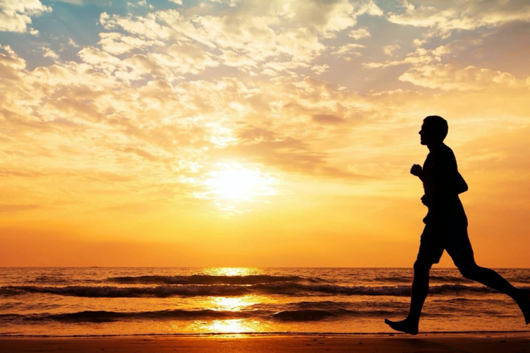 Silhouette of a person running on the beach at sunset.
