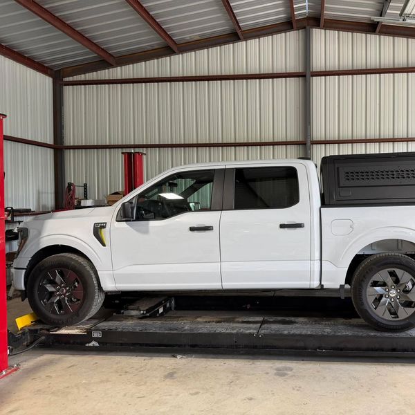 White pickup truck with a black canopy parked inside a garage.