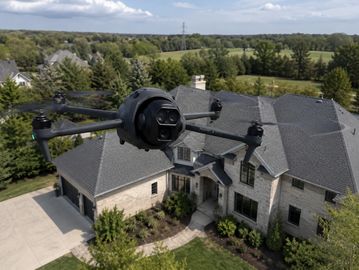 A DJI Mavic 4 Pro drone flying over a suburban house.