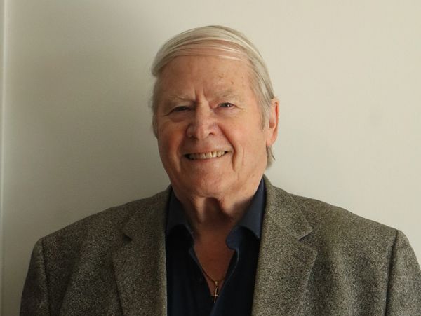 Smiling elderly man in a gray blazer and navy shirt.