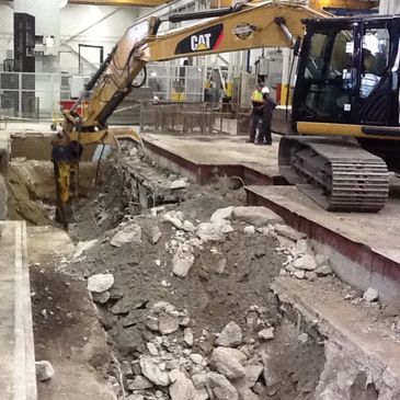 An excavator digging a trench for a concrete machine foundation in a manufacturing facility