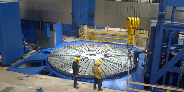 Construction workers working to set up heavy machinery in a manufacturing facility. 