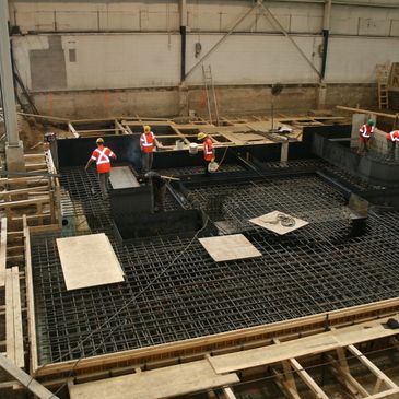 Construction workers setting up a rebar system for pouring a concrete machine base in a facility